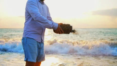 An unrecognizable man scatters ashes over the sea from a cremation urn close up Stock Footage 246745533