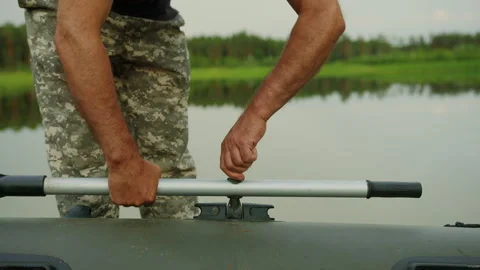 An unrecognizable man screws oars to an inflatable boat on the shore of the lake Stock Footage 248444728