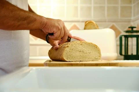 Unrecognizable man standing at table in kitchen and cutting bread with knife Foto stock