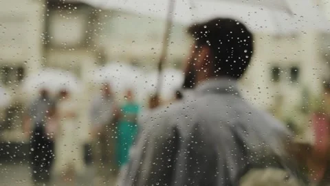 Unrecognizable man stands in the rain under an umbrella, view through drops from Stock Footage 318064996