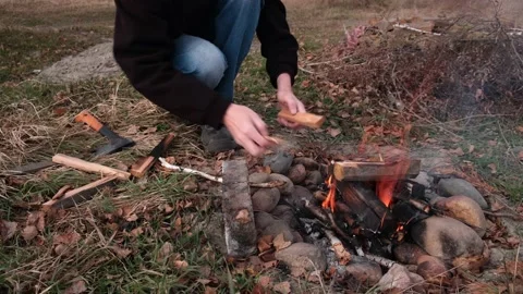 An unrecognizable man throws wood on the fire to warm up and cook food. 4K. Stock Footage 201478371