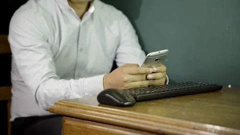 Unrecognizable Man types using computer keyboard and checks cell phone in office Video stock 275350944