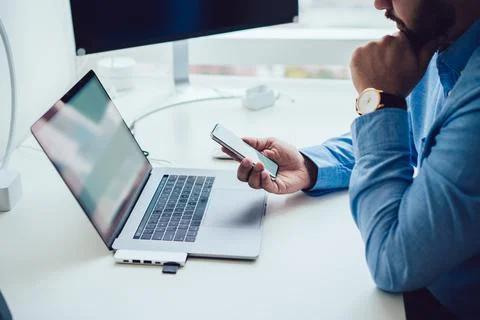 Unrecognizable man using smartphone while working on laptop Stock Photos