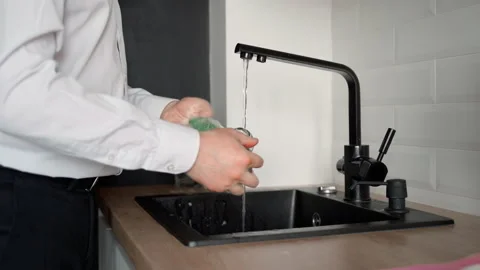 An unrecognizable man washes a mug in the kitchen sin Stock Footage 153283576