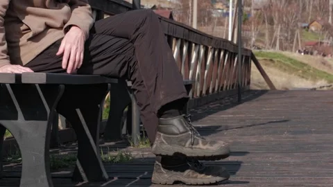 Unrecognizable man in work clothes and worn shoes approaches bench and sits down Stock Footage 246729687