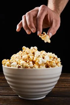 Unrecognizable man's hand taking a delicious caramel popcorn from a white bow Stock Photos