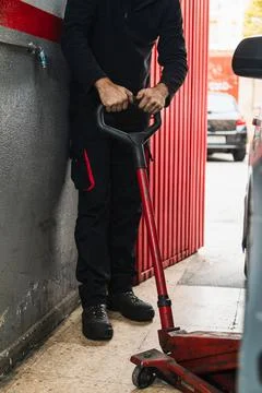 Unrecognizable mechanic using a jack to lift car. Automobile mechanics concep Stock Photos