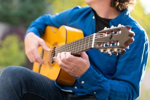 Unrecognizable middle-aged man playing Spanish guitar sitting on park bench Stock Photos