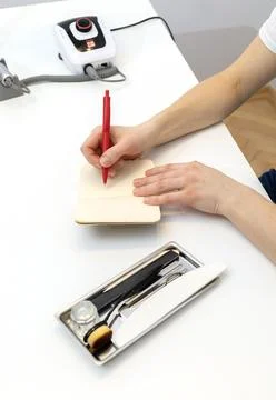 Unrecognizable nail master makes notes in notebook with pen, sitting at Stock Photos