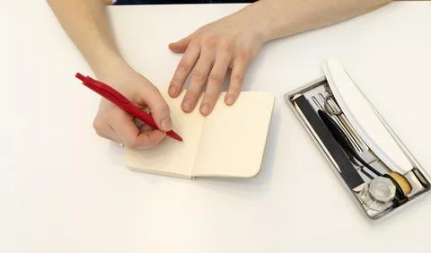 Unrecognizable nail master makes notes in notebook with pen, sitting at Foto stock