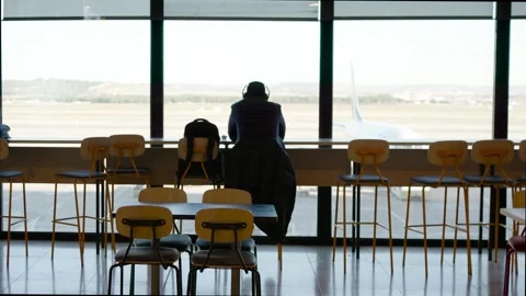 Unrecognizable passenger seated at bar in front of huge airport windows with Stock Footage 309061980