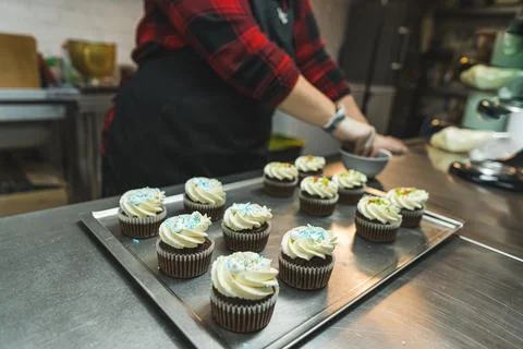 Unrecognizable person at a bakery kitchen decorating muffins with colorful Stock Photos