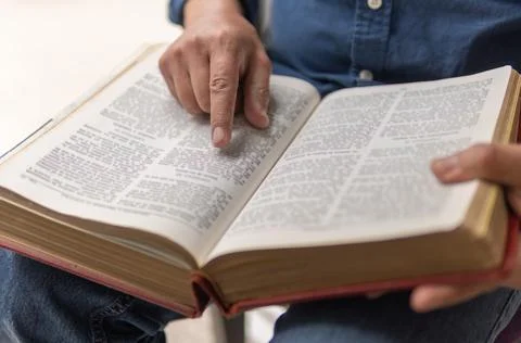 Unrecognizable person sitting studying the bible with selective focus on his Stock Photos