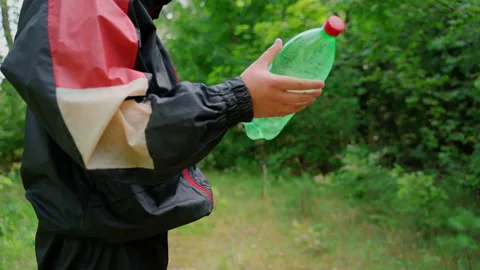 Unrecognizable person throw plastic bottle in nature. Forest pollution Stock Footage 158119420