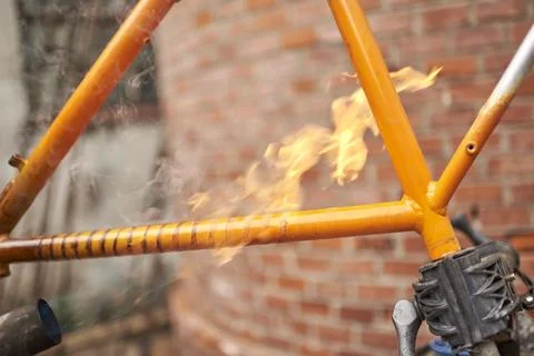 Unrecognizable person using a blowtorch to remove the paint of a bicycle fram Stock Photos