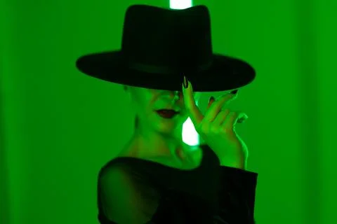 Unrecognizable sexy woman runs finger across brim of hat in dark neon studio Stock Photos