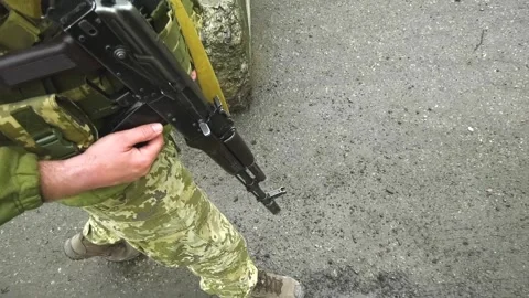 An unrecognizable soldier walks down the road with a machine gun down. Russo Stock Footage 240179177