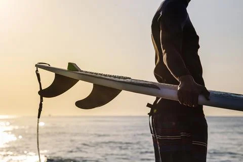 Unrecognizable surfer preparing to surf on the beach at sunrise Stock Photos