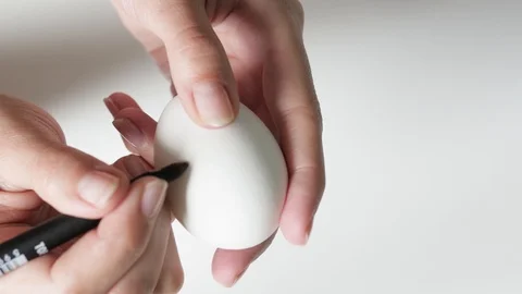 An unrecognizable woman holding a marker draws patterns in black on an egg on Stock-Footage 107932953