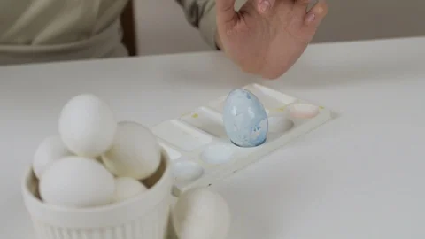 Unrecognizable woman paints Easter eggs with a brush. On the table is a glass of Stock Footage 86987863