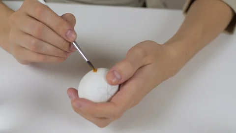 Unrecognizable woman paints Easter eggs with a brush. On the table is a glass of Stock Footage 86990524