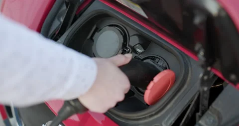 Unrecognizable woman plugging in electric car charging station. Luxury red Stock Footage 194490053