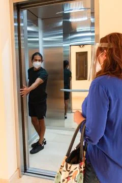 Unrecognizable woman waiting for elevator while man holds the door Stock Photos