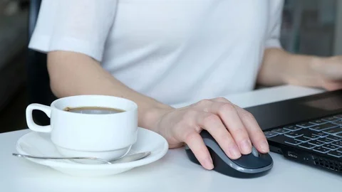 Unrecognizable woman's hands working on laptop keyboard and drinking coffee Stock Footage 129353899
