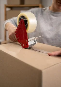 Unrecognizable worker sealing cardboard parcel box with tape dispenser. app.. Stock Photos