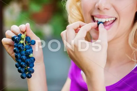 Unrecognizable young blond woman holding and eating blue grapes Stock Photos