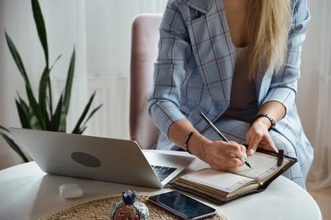 Unrecognizable Young woman making notes in notebook sitting at workplace at home Stock Photos