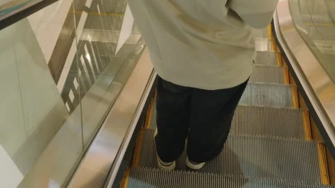 Unrecognized person riding down an indoor escalator in a shopping center. Video stock 343375192