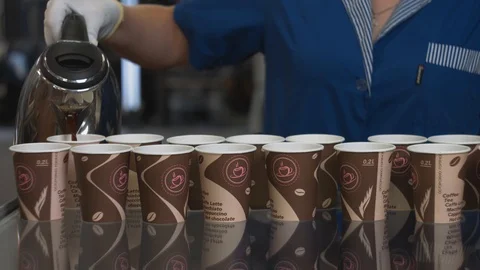 Unrecognized plant worker in blue uniform tests paper cups by pouring hot coffee Stock Footage 93338921