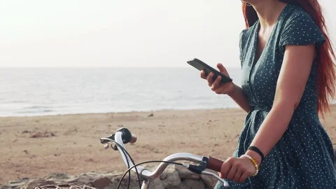 Unrecognized red hair female using her smartphone standig with bicycle at sea 4k Video stock 106915609