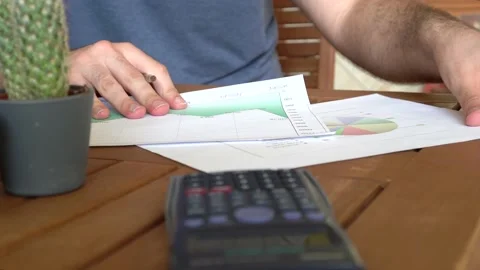 Unrecognized young man analyzing charts on desk with a calculator while worki Stock Footage