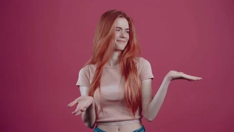 Unsatisfied redhead for 20 years, in a pink casual T-shirt, isolated on a pink 库存影片 150367657