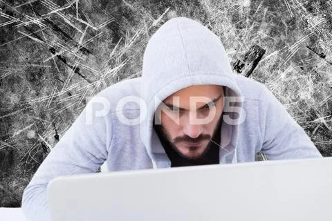 Unsmiling cyber criminal is looking at the screen of the laptop against grey, Stock Photos