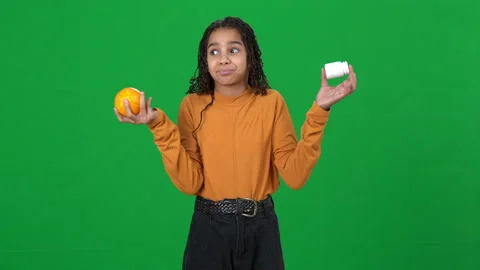 Unsure African American teen girl on green screen holding drugs and orange Stock Footage