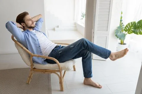 Untroubled millennial single man relaxing on chair in fashionable home Stock Photos
