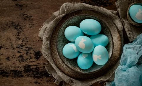 Unusual Easter on dark old background. Ceramic brown bowl with blue eggs with Stock Photos