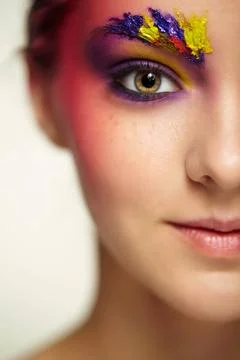 Unusual female face art make-up with paint on brows and around eyes. Close... Stock Photos