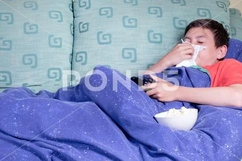 Unwell young teenage boy wrapped in a duvet on a sofa Stock Photos
