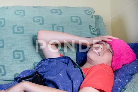 Unwell young teenage boy wrapped in a duvet on a sofa Stock Photos