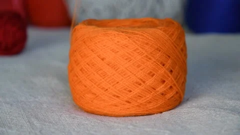 Unwinding a bobbin with thin orange yarn on a light background Stock Footage 137312621