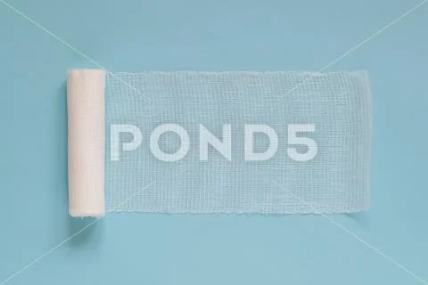 Unwound roll of white sterile medical bandage for dressing wounds on a blue Stock Photos