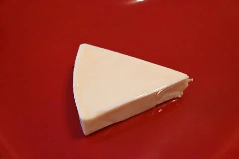 Unwrapped processed cheese wedge on a red surface Stock Photos