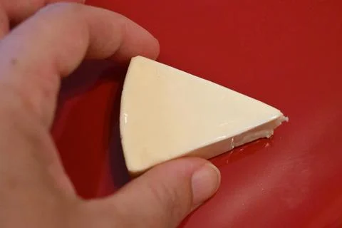 Unwrapped processed cheese wedge on a red surface Foto stock