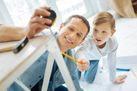 Upbeat boy checking the length of a table leg Stock Photos