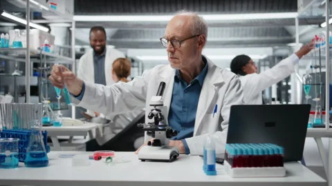 Upbeat elderly lab professional investigating blue liquid polymer properties Stock Footage 326558128