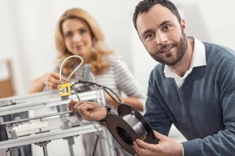 Upbeat engineer posing while replacing filament in 3D printer Stock Photos